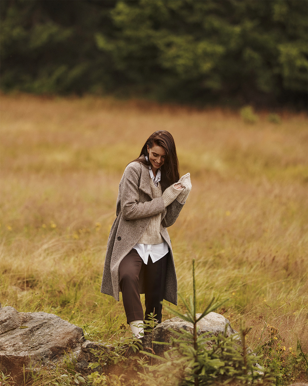 žena stojící na mýtině v elegantním kabátu v kostkovaném vzoru