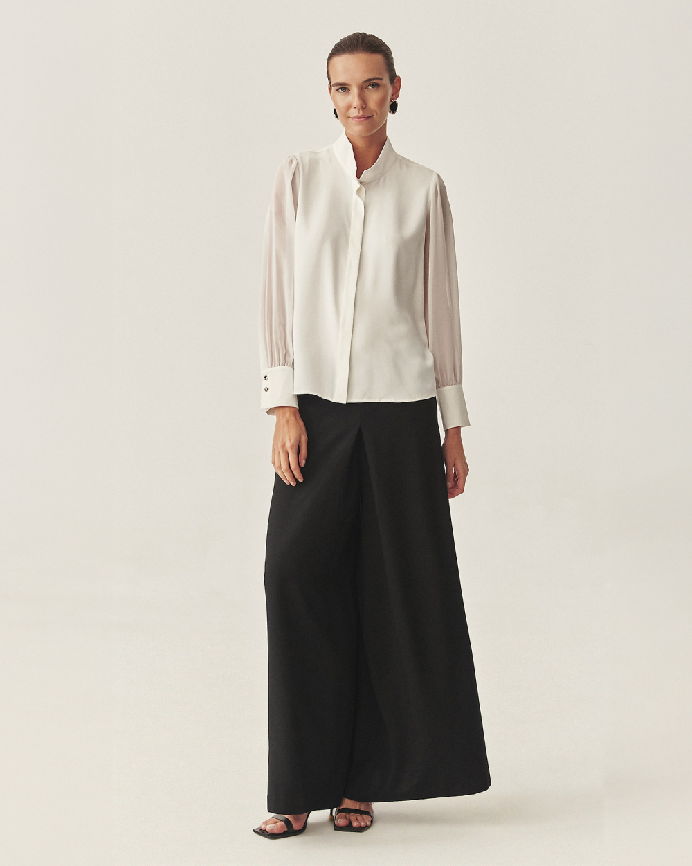 o femeie îmbrăcată într-o cămașă albă elegantă și pantaloni negri cu croi larg