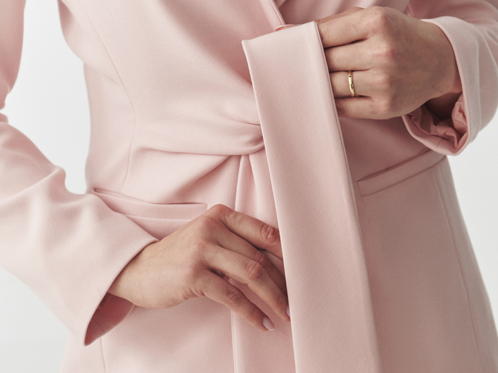 Detailní záběr bílé blůzy s růžovou květinovou broží na rameni