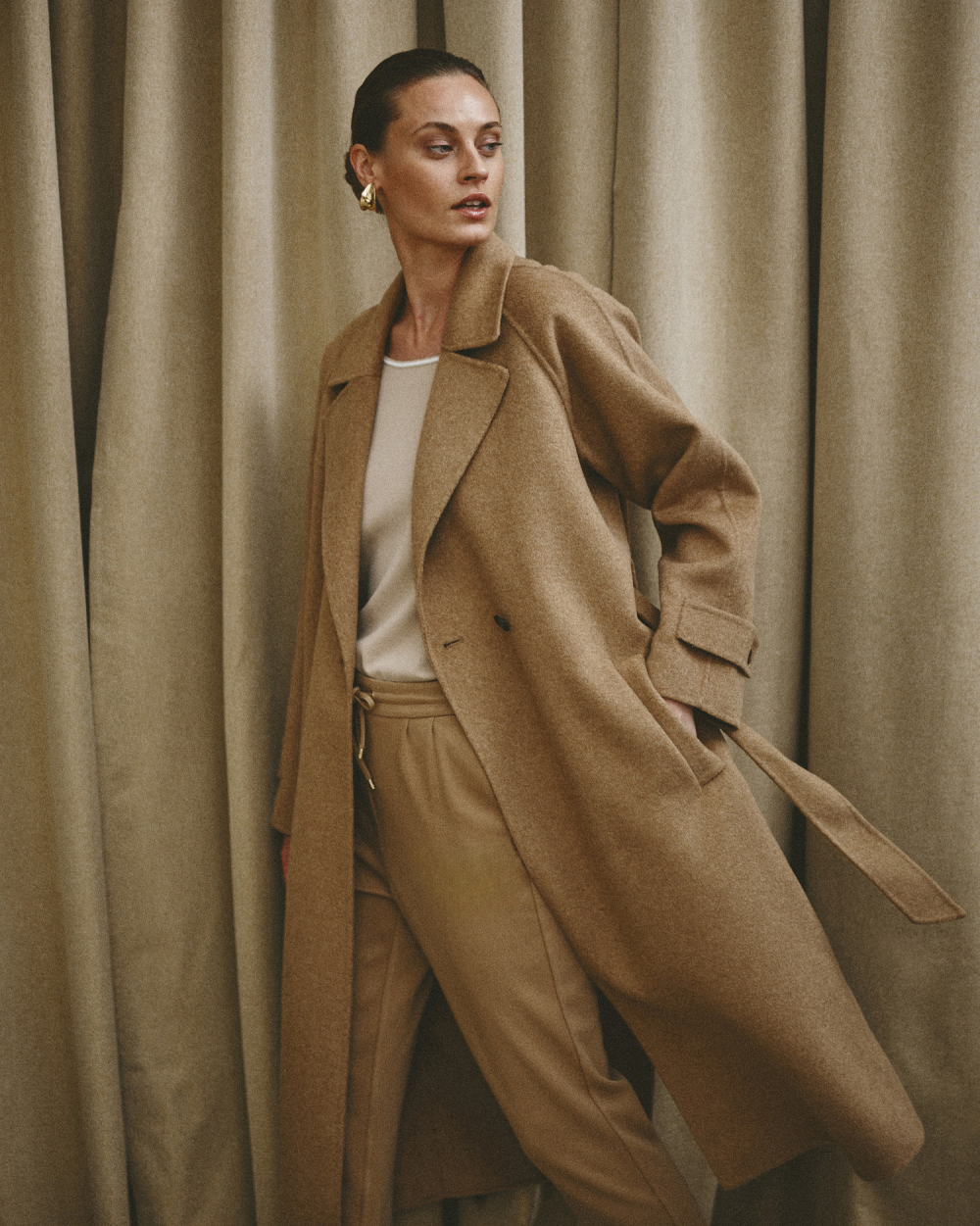 stojąca kobieta trzymająca dłoń w kieszeni długiego płaszcza