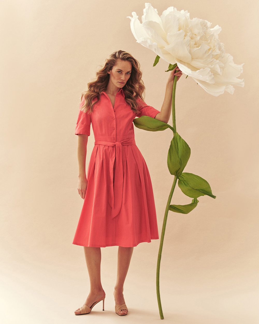 kobieta trzymająca ogromny kwiat, ubrana w rozkloszowaną sukienkę 