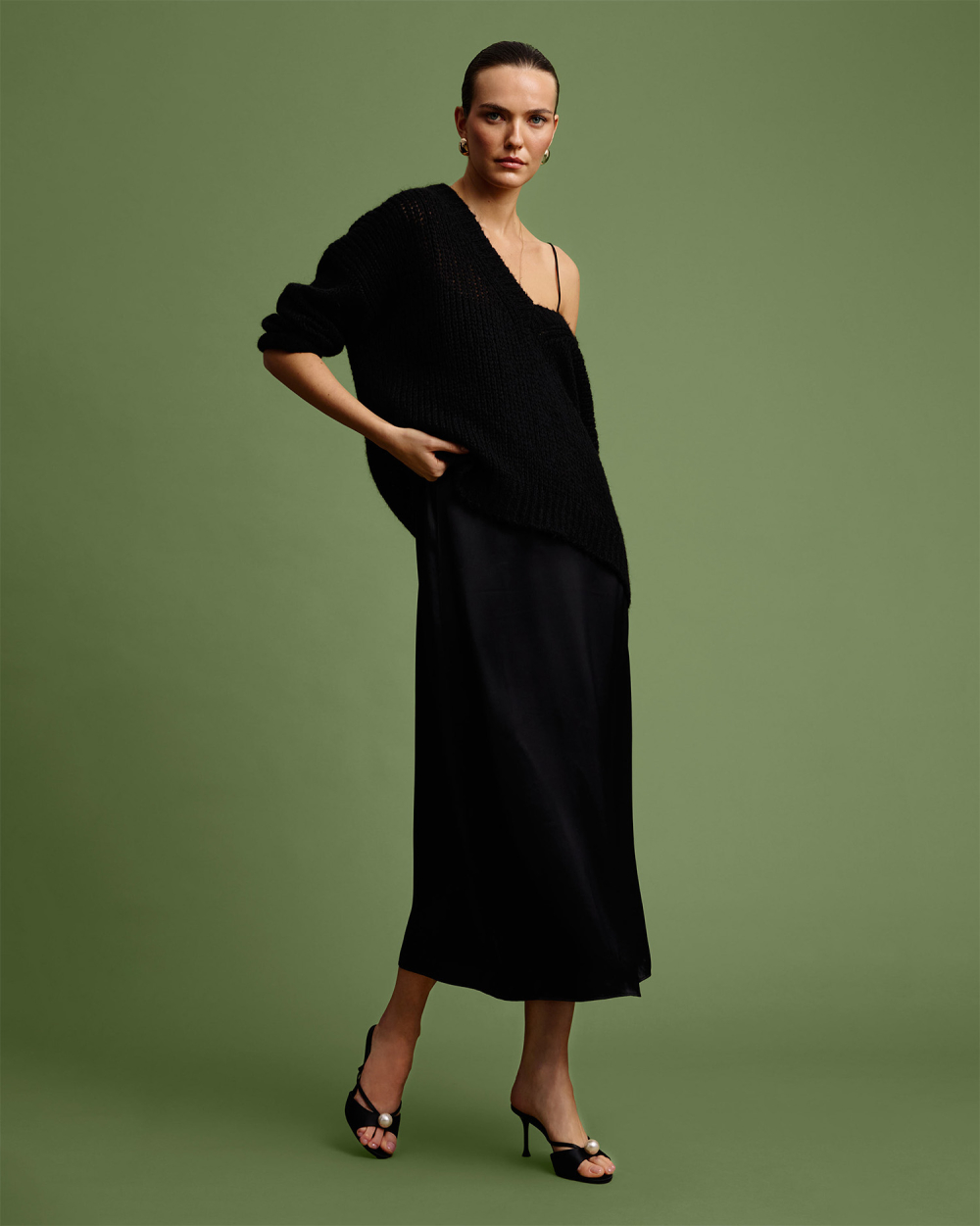 Modelka v černém oversize svetru. Stylizace s odhaleným ramenem.