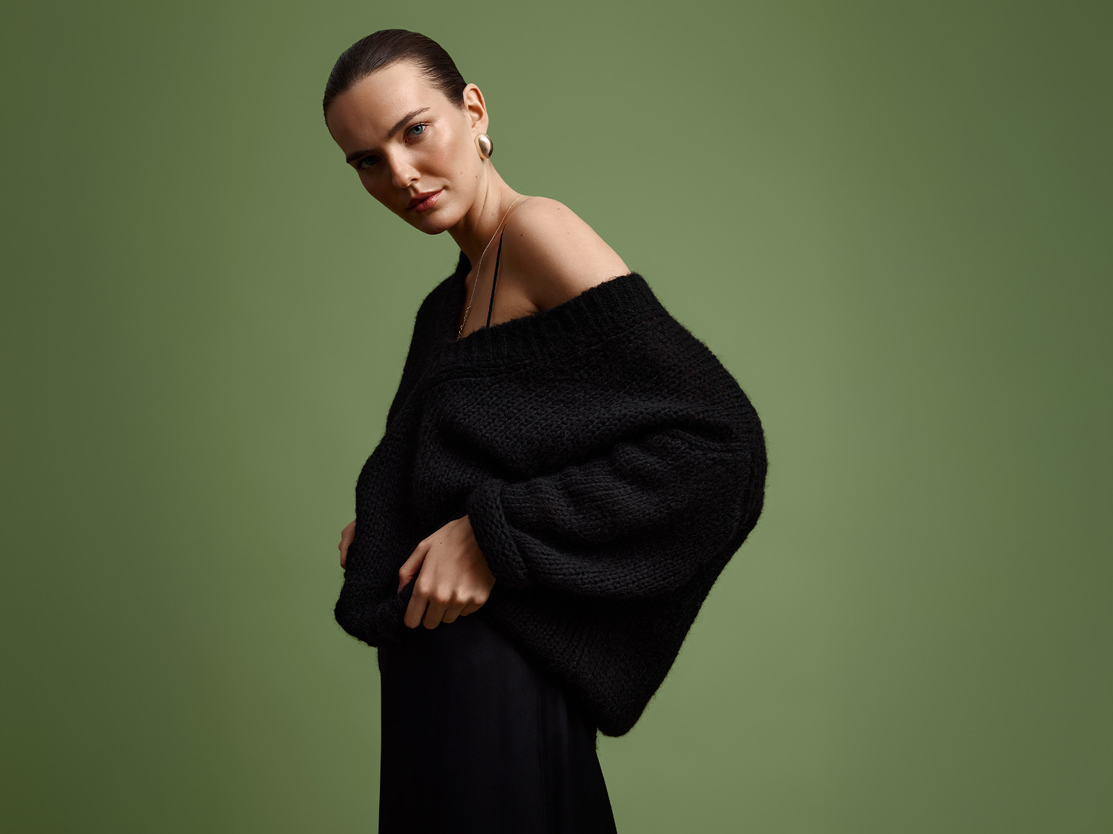 Modelka v černém oversize svetru. Stylizace s odhaleným ramenem.