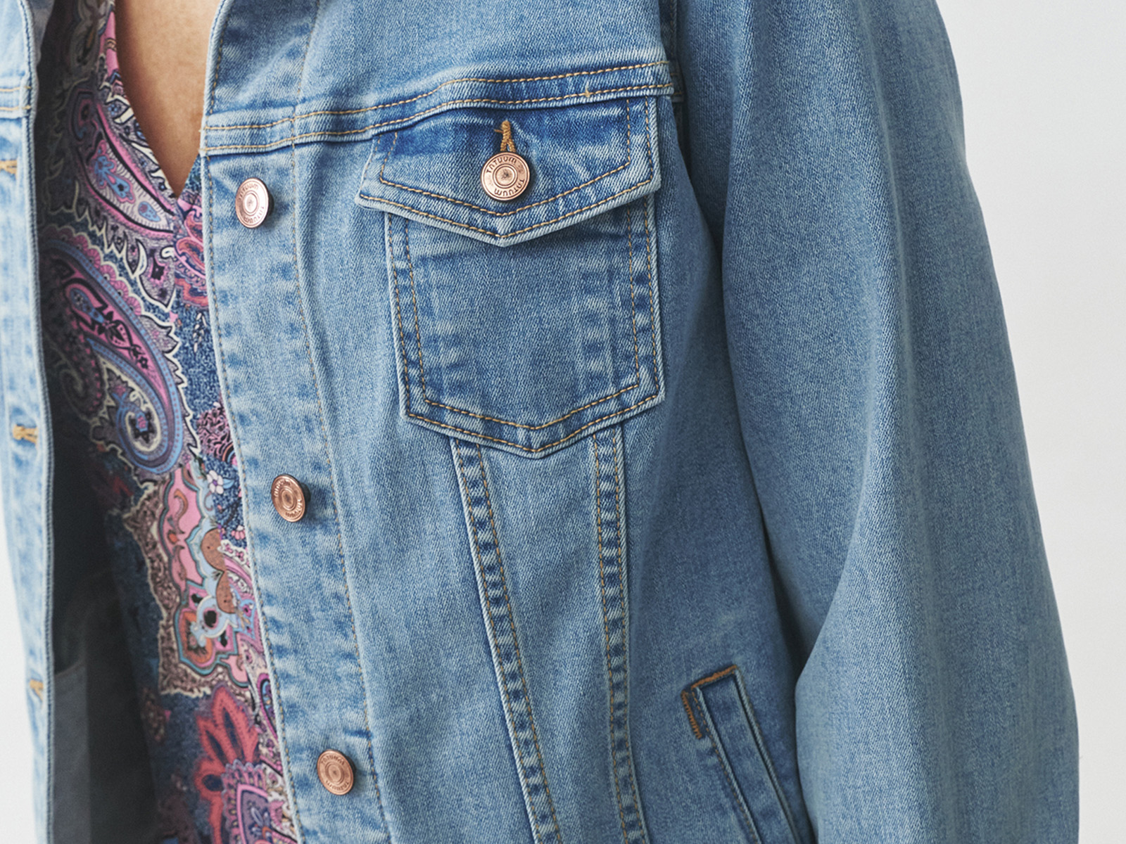 Detaliu al unei jachete din denim clasic purtate peste o bluză cu imprimeu paisley.