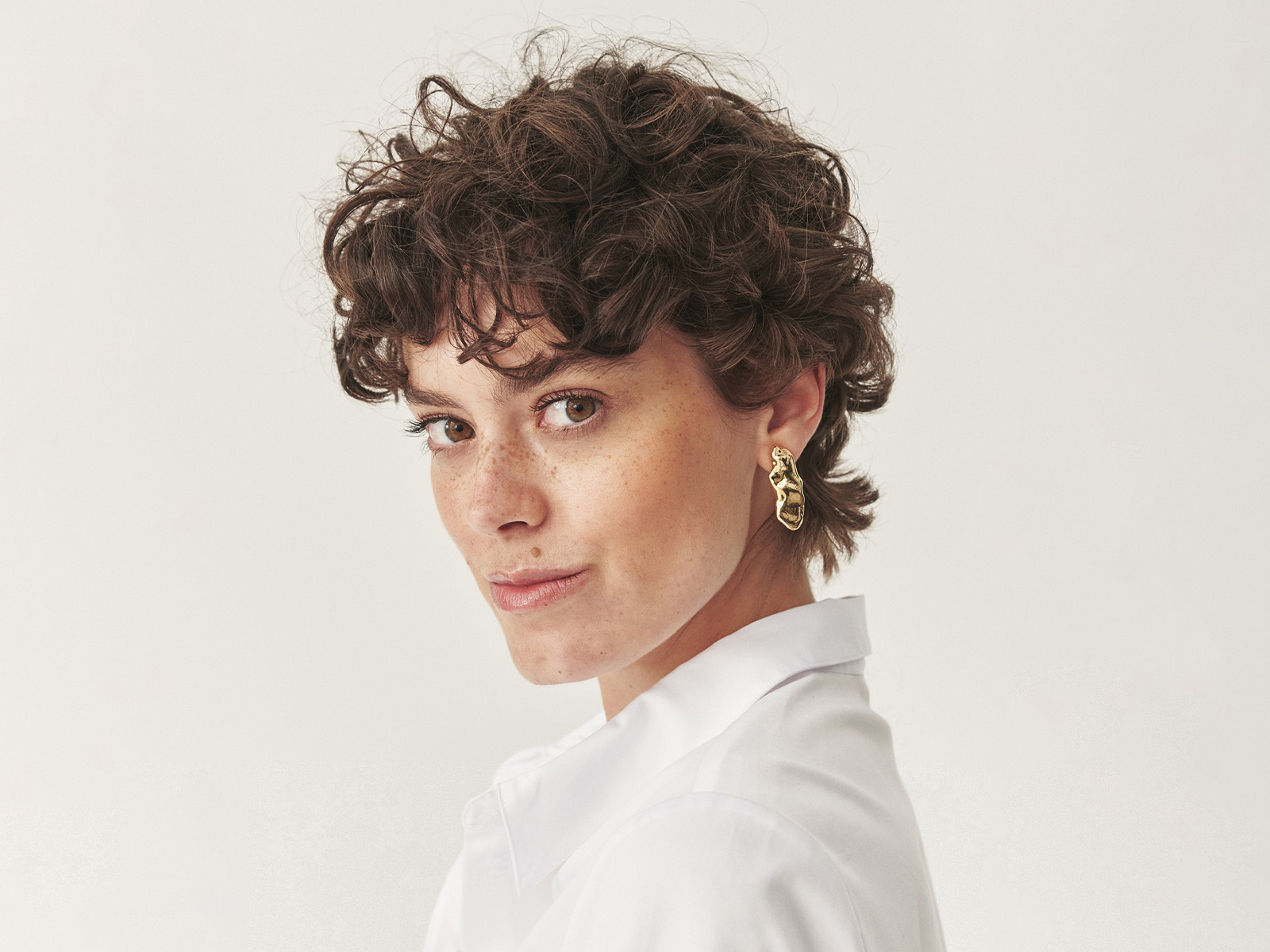 Zbliżenie na twarz kobiety w białej koszuli i eleganckich złotych kolczykach