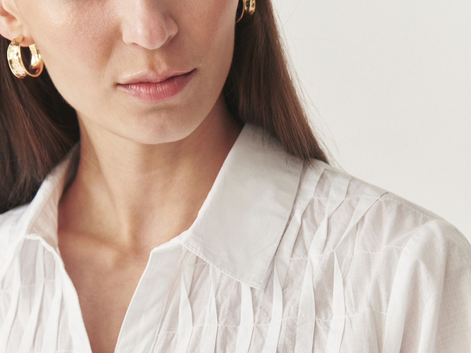 Zbliżenie na kobietę w białej koszuli i eleganckich złotych kolczykach
