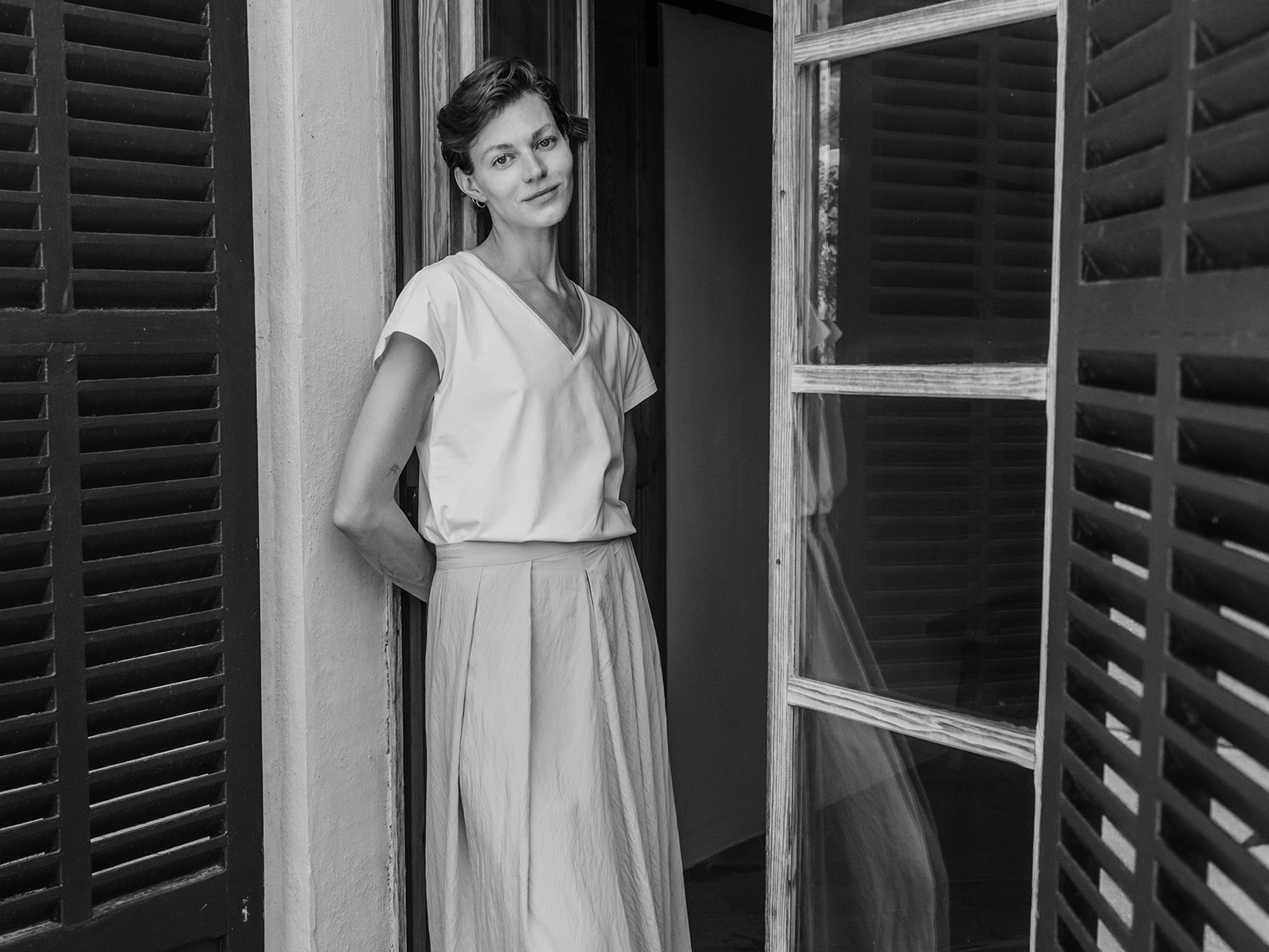 Žena v letním kompletu se sukní, stojící ve dveřích, černobílá fotografie