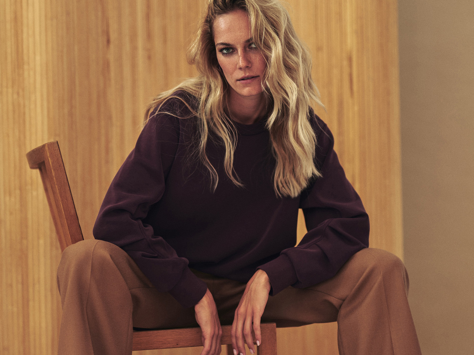 modelka sedící na židli oblečená v bordovém svetru a béžových elegantních kalhotách