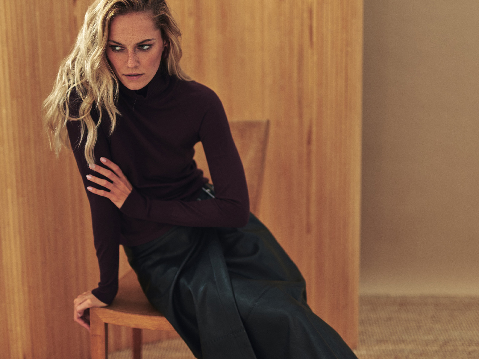 Modelka patrząca w bok ubrana w bordowy gold i elegancką, czarną spódnicę