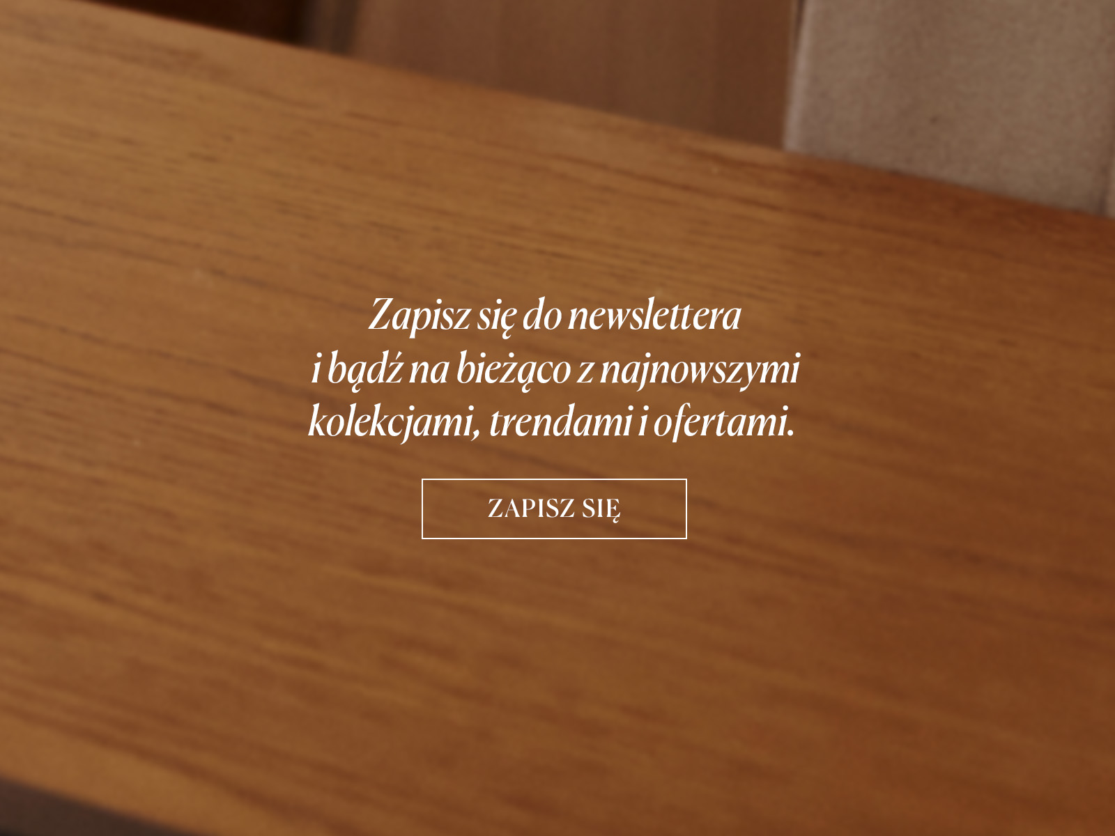 Zbliżenie na drewniany blat stołu z napisem zachęcającym do zapisu na newsletter.
