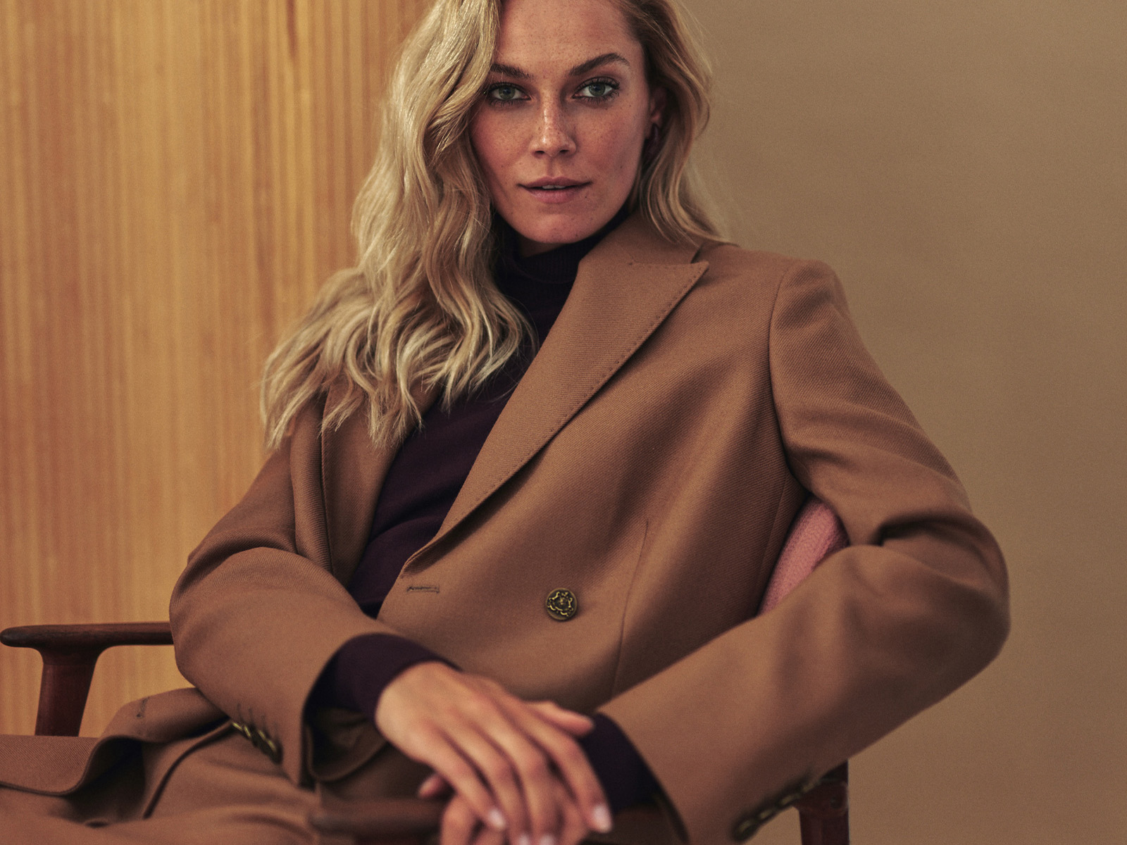 o femeie așezată pe un scaun, îmbrăcată într-un costum bej elegant