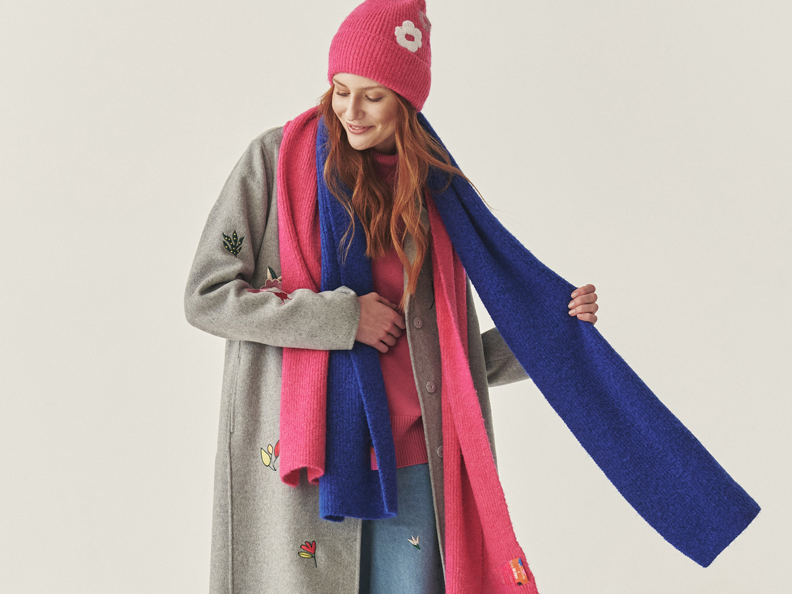 žena v sivom kabáte, ružovom klobúku s kvetinou a modrom zimnom šále