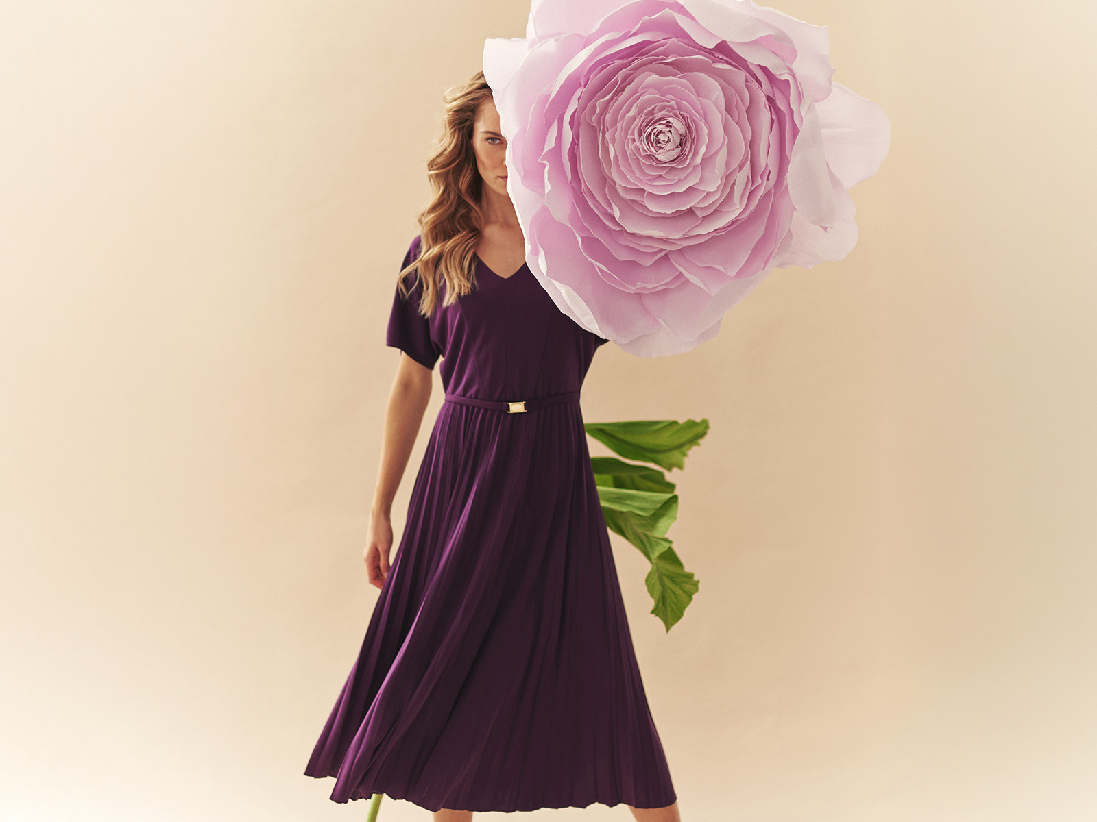 kobieta w długiej plisowanej sukience oraz wielki kwiat